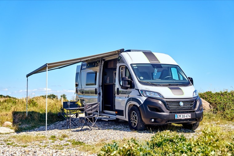 Autocamperen med markisen slået ud og campingstole klar ved kysten