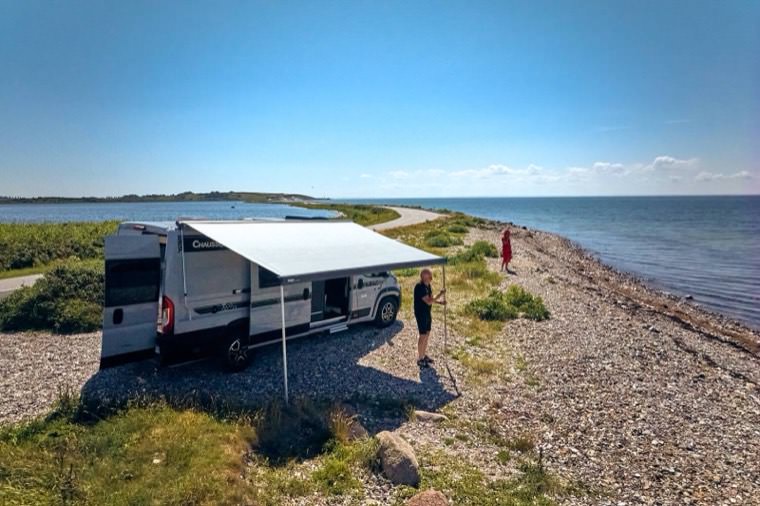 Autocamperen ved vandkanten med markisen slået ud en sommerdag
